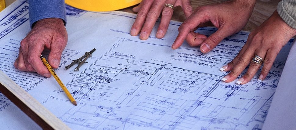 Hands marking up a set of building drawings with a pencil and dividers.